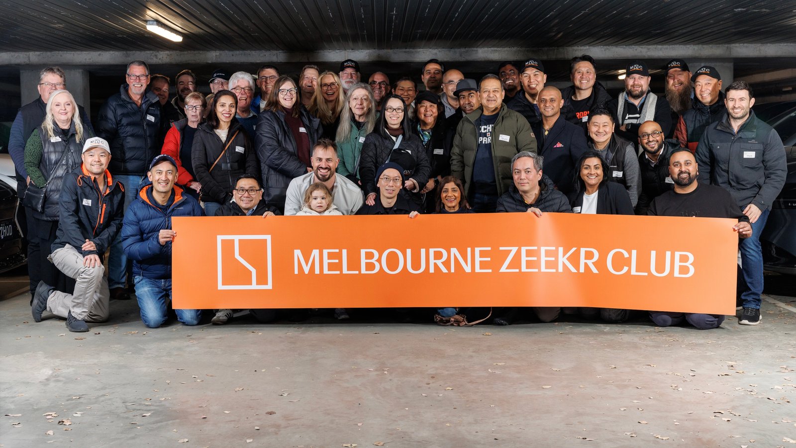Melbourne ZEEKR Club members behind their orange club banner